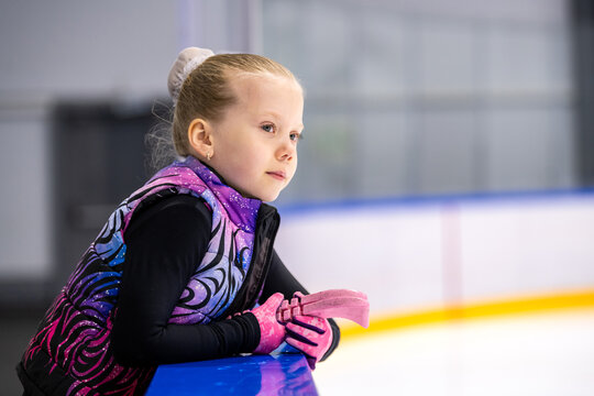 girl figure skater watches training session at edge of  ice rink.