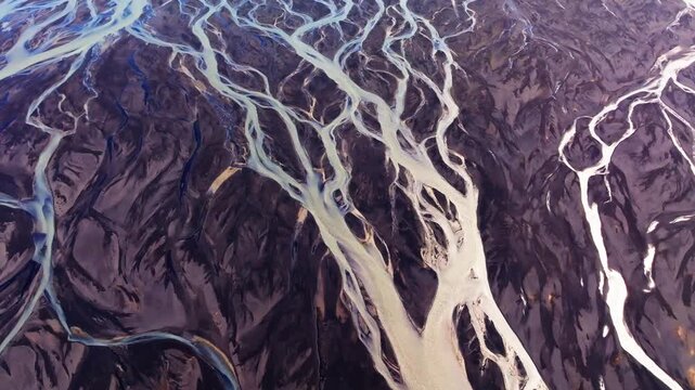Abstract drone view of braided glacial river delta and black sand in Iceland. Top-down aeria footage of intricate glacial river channels carving organic patterns through dark volcanic sand.