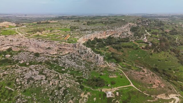 At Malta's Dingli Cliffs, a drone captures the limestone cliffs and surrounding rural farmland with rocky terrain, vegetation, and coastal Mediterranean landscape in winter.