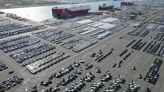 High rear drone view frames three Drive Green car ships and the giant vehicle lot.