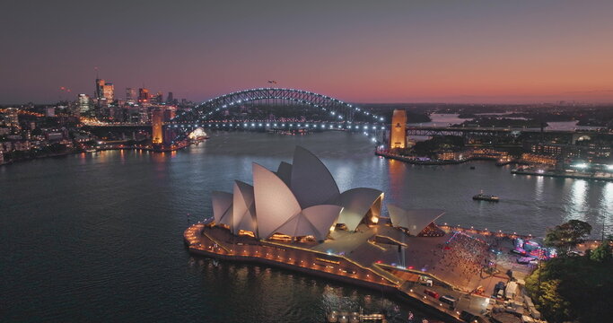 Sydney, Australia - 01.24.2023: Sydney Opera House with Sydney Harbour Bridge in background illuminating night lights, cityscape view with colorful sky and illuminated buildings. Aerial drone footage