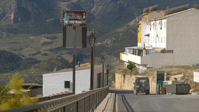 An old 4x4 off-road car drives down a descriptive mountain village road next to white houses.