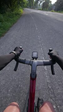 A cyclist's view of a road ride, showcasing handlebars, a bike computer, and a scenic route with greenery.