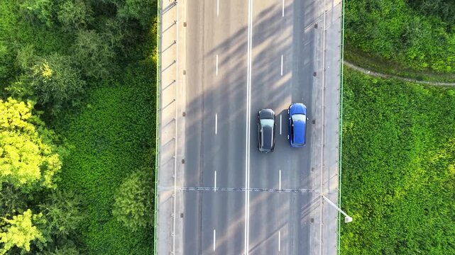 Aerial view of multiple cars traveling on a highway surrounded by lush green vegetation, showcasing the flow of traffic and the natural landscape in the background