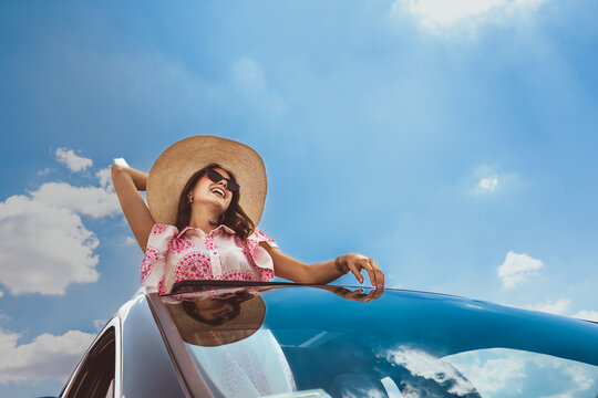 Young woman in sun hat enjoying convertible road trip under bright blue sky