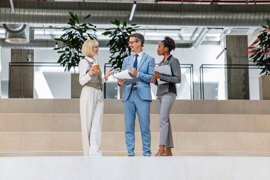 Business colleagues discussing documents in modern office atrium during informal meeting