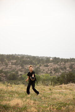 Boy catching baseball in field in mountains