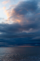 Fototapeta premium Dark, textured clouds reflect golden sunset over still sea