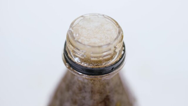 A top view close-up of a cola bottle top with foam bubbling at the opening against a white background.