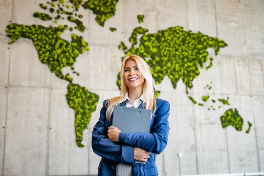 Businesswoman standing confident with clipboard in front of green world map symbolizing global sustainability