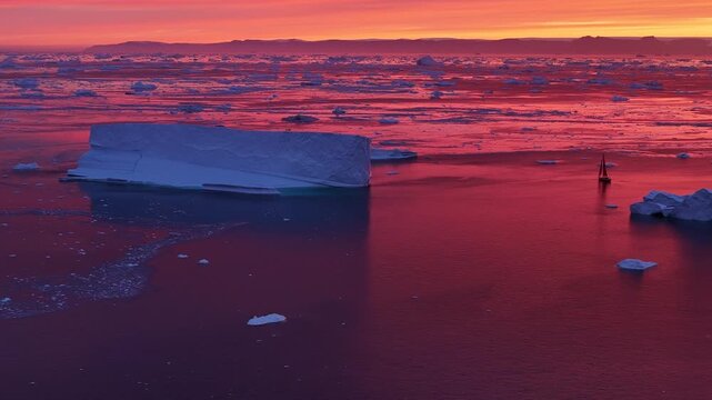 Lone sailboat sailing through an icy sea at sunset