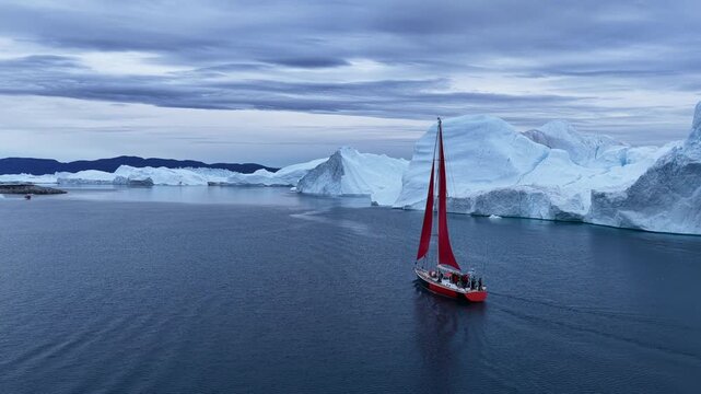 Bright red sailboat navigating by massive icebergs