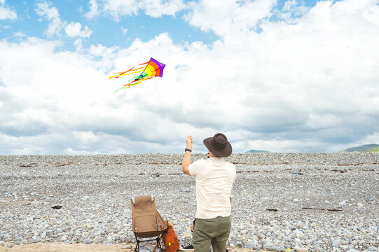 Man flying a colorful kite on a pebble beach