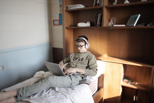 Teenage boy with headphones using laptop in bed
