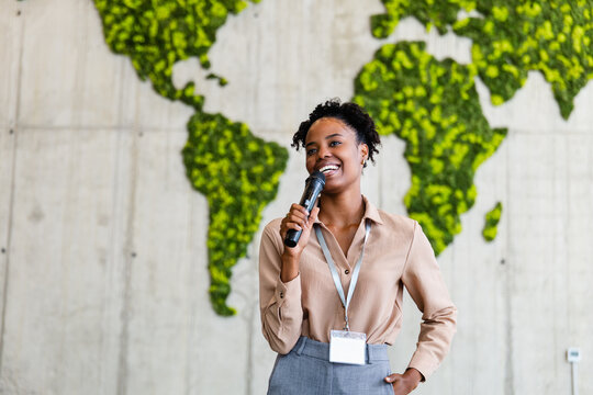 Black woman business speaker presenting at conference with world map backdrop and confident smile