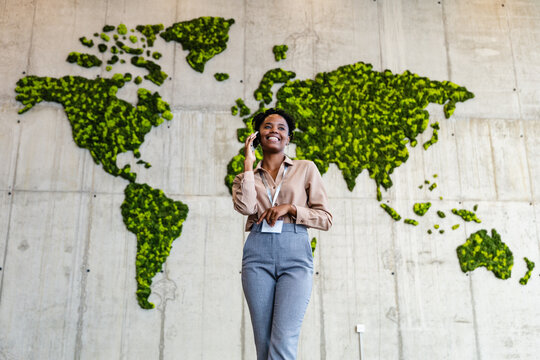 Businesswoman talking on phone in front of green world map wall, African American professional
