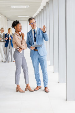 Two colleagues discussing project strategy in modern corporate office hallway