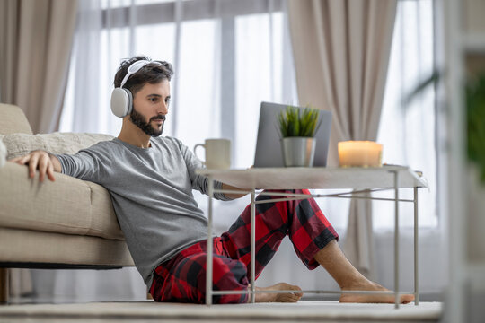 Caucasian American man relaxing at home with headphones and laptop in cozy living room