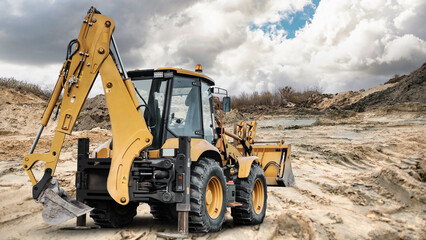A universal excavator loader is on a construction site digging and moving earth under a cloudy sky during daytime near piles of dirt © Anoo