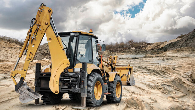 A universal excavator loader is on a construction site digging and moving earth under a cloudy sky during daytime near piles of dirt