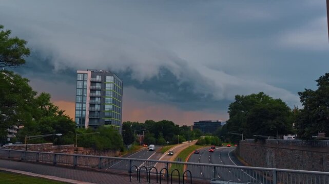 Storm clouds over urban highway traffic in Washington, DC, curved lanes, cars, trees and towers appear below.