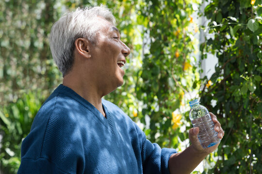 elderly asian man feeling refreshing after drinking water from bottle while relaxing on park
