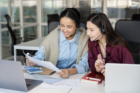 Smiling coworkers in headsets reviewing business papers