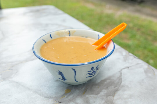 A small ceramic bowl containing a smooth, creamy brown dessert called "bubur gandum" in Malaysia. It is made from pearl wheat, palm sugar and coconut milk.