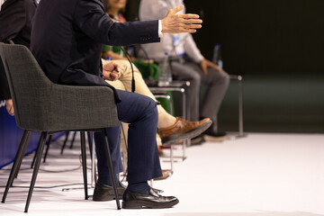 Fototapeta premium Business panel discussion with gesturing speaker and microphones at corporate conference, leadership forum and executive event. Round table political meeting with copy space.