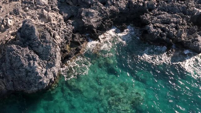 Waves splashing on rocks on the Crete island coastline, drone aerial view
