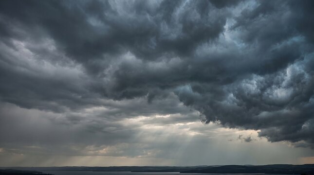 Moody overcast sky filled with heavy textured dark clouds and faint sunbeams over a distant water horizon