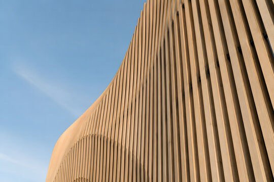 Parametric oak timber wave facade with flowing architectural geometry against a clear blue sky