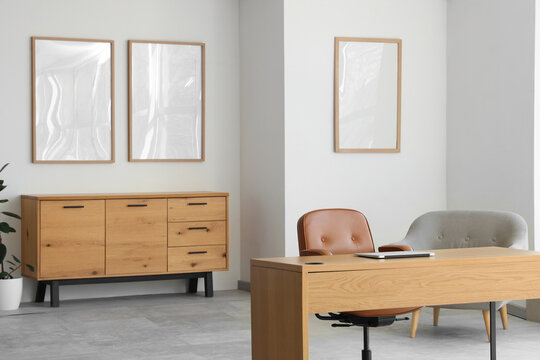 Interior of light office with blank frames, commode and workplace