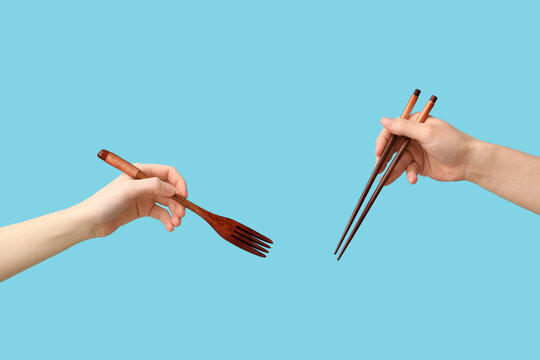 Hands holding wooden fork and chopsticks on blue background