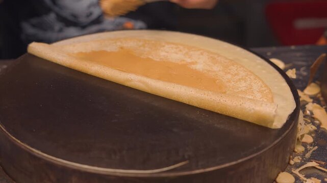 street food vendor preparing fresh crepe with peanut butter and chocolate spread, fresh dessert crepe cooking on hot griddle with choco drizzle at street food market 4k