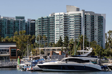 Luxury yacht moored at Marina del Rey harbor with modern waterfront residential towers under clear blue California summer sky © sjv156