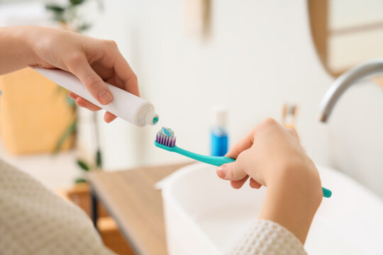 Person applying toothpaste on toothbrush in bathroom