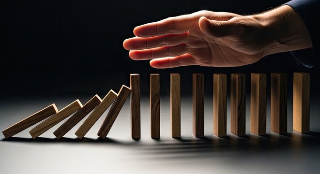 Close-up hand halting wooden domino chain reaction.