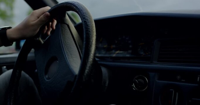 Close up of hands holding and turning a black steering wheel inside a classic car dashboard interior