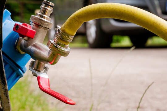 Close up of brass ball valve with red handle connected to garden hose and water filter system on outdoor background
