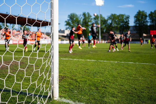 Action on the Soccer Pitch With Players in Motion Seen Through a Stadium Goal Net and Focusing on the goalpost.