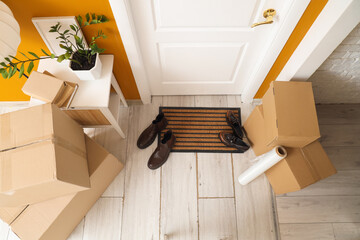 Naklejka premium Doormat with shoes and cardboard boxes in hallway on moving day, top view