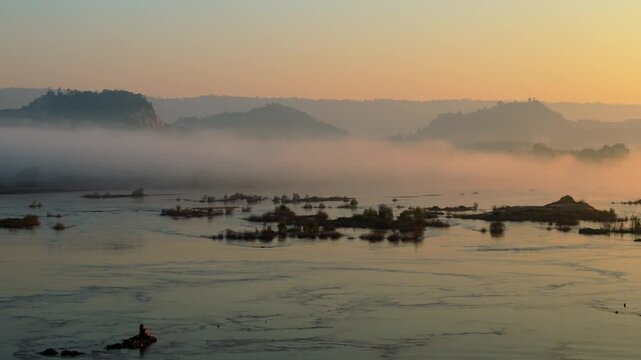 Birds-eye view of beautiful golden sunrise light reflecting on a misty, wide river landscape in Nong Khai Province with exposed boulders