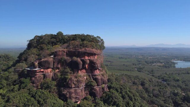 Drone shot capturing the seven levels of hand-built wooden staircases surrounding a massive sacred rock formation temple wat phu tok in the jungle