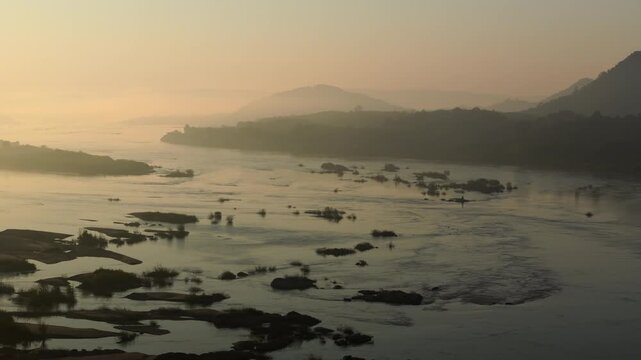 Birds-eye view of beautiful golden sunrise light reflecting on a misty, wide river landscape in Nong Khai Province with exposed boulders