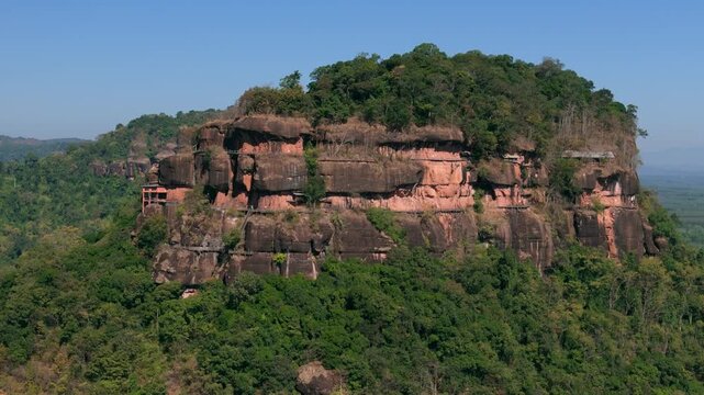 Drone shot capturing the seven levels of hand-built wooden staircases surrounding a massive sacred rock formation in the Thai jungle