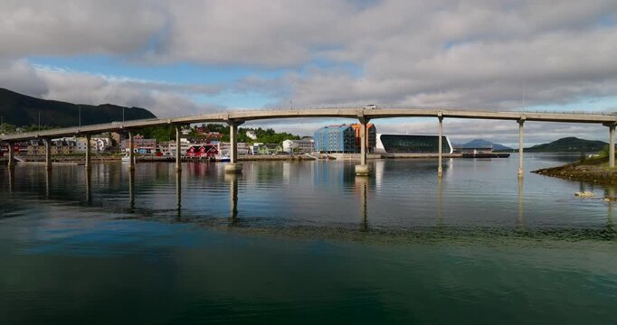Aerial establishing dolly of Stokmarknes waterfront bridge and harbor reflected in calm water, drone background