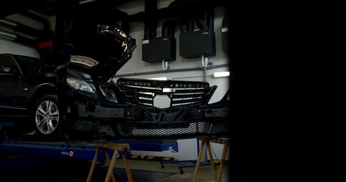 Wide shot of an auto repair workshop with a black car on a lift and dismantled front parts on stands