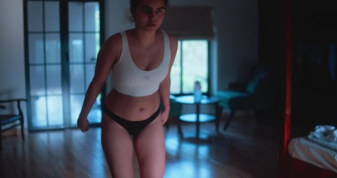 Woman in sportswear stretching arms behind back in softly lit home interior