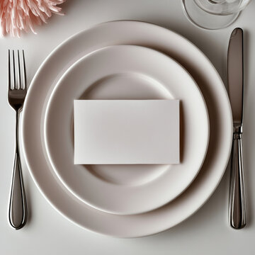 Elegant table setting with white plates, blank card, silver cutlery, glass, and soft pink flower, perfect for formal dinner event